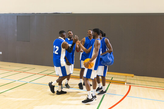 African american male basketball players high-fiving on court holding basketball, duffel bag