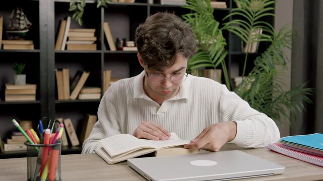 Student boy absorbed in studies, doing his homework, preparing for university admission, sitting at the desk, using laptop for online learning, acquiring new knowledge, improving his English skills.