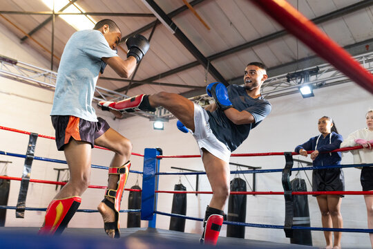 Diverse fighters sparring in boxing ring at gym in gloves and shin guards near punching bags