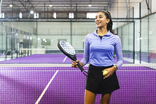 Indian female athlete in sportswear serving near net on purple padel court with racket and ball