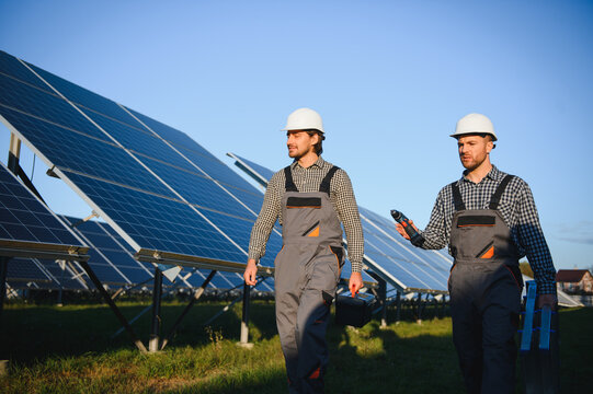 Portrait of two professional workers in uniform and helmets working in a field of solar panels