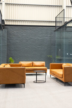 Mustard leather sofas sitting around black coffee table in office lounge with partitions, plants