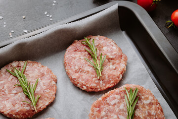 Four raw pork burger patties with rosemary ready for grilling, top view with ingredients