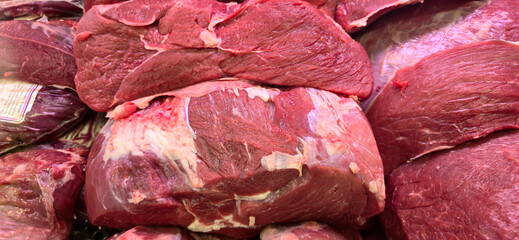 Several large cuts of raw beef with visible fat layers displayed on a butcher’s counter under bright lighting. Uncooked meat, freshness.