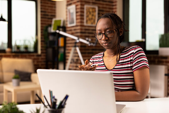 Focused black woman speaking with team during virtual meeting on laptop. African american female employee working from home, participating in video conference with coworkers on personal computer.