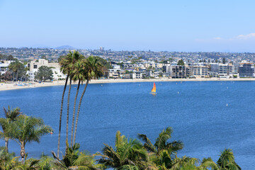 Fototapeta premium Birds-eye view of beachfront resorts, hotels and rental houses crowded at sandy edge of Sail Bay under summer blue sky with rare white clouds, San Diego, California
