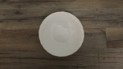 Top view of round white ceramic plate placed on wooden background, kitchenware concept