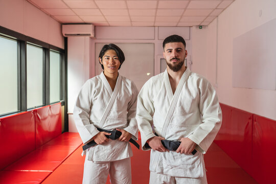 Two judo athletes posing in training room wearing white kimonos and black belts