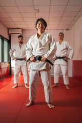 Martial arts athletes posing in dojo wearing white kimonos and black belts