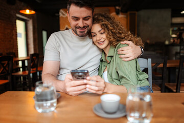 Happy couple looking at smartphone while having coffee in a cafe