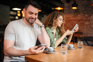 Young couple looking at their smartphones while having coffee at the bar