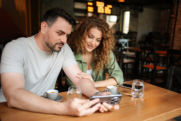 Couple looking at smartphone and drinking coffee in cafe
