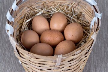 Basket filled with brown chicken eggs on straw.
