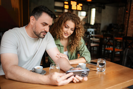 Couple looking at smartphone and drinking coffee in cafe