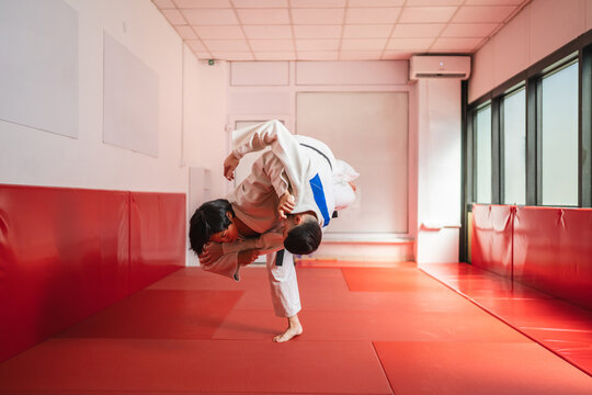 Two judo athletes training together, performing a throw in a gym - Powered by Adobe