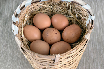 Basket filled with brown chicken eggs on straw.