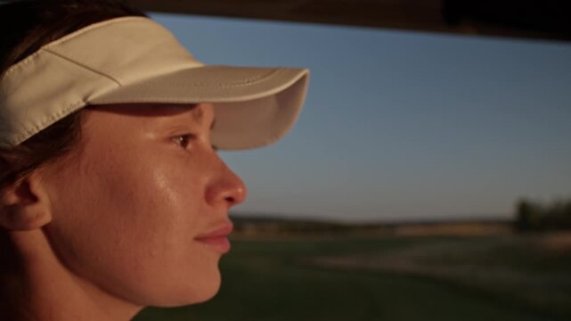 Young woman golfer in visor hat relaxes in golf cart closeup