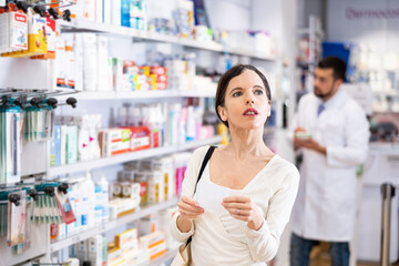 Woman chooses medical products in pharmacy, checking the list on a piece of paper