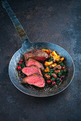 Barbecue dry aged beef steak - roast beef medium roasted, sliced with wild mushrooms, chestnuts, greens and cranberries in iron skillet pan