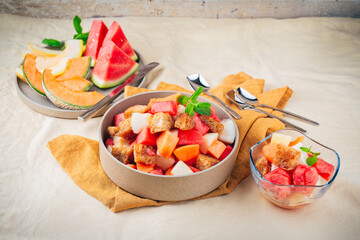 Homemade fresh melon fruit salad with waer melon, honey melon and butter roasted bread croutons served as close-up in a design plate