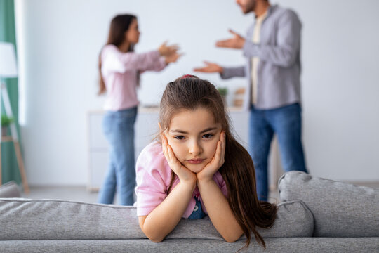 Family crisis and relationship problems. Upset girl looking at camera while her angry parents fighting on the background, depressed child feeling lonely, selective focus