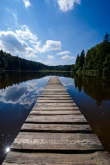 Obraz premium Wooden pier at the peaceful lake with at sunny summer day with blue sky and forest background