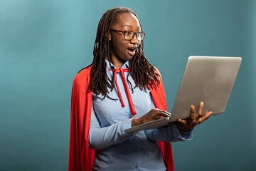 Shocked african american woman in a red cape stares at her laptop with wide eyes. Black female...