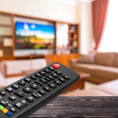 Close up of a television remote control in the foreground with a blurred living room background.