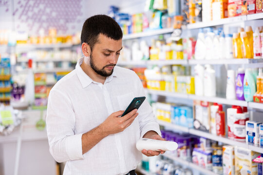 Caucasian man using his smartphone to take picture of skin care product in pharmacy.