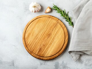 A wooden cutting board with garlic and rosemary on a textured gray surface, complemented by a light-colored towel.