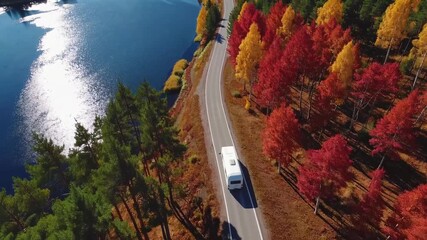 Motorhome travels along scenic river with autumn trees reflecting bright colors