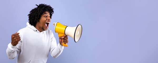 Emotional black adolescent shouting into megaphone, making announcement over violet studio...
