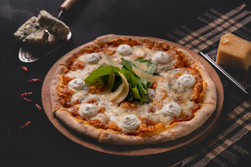 Delicious four cheese pizza on dark background. Homemade Italian four cheese pizza. Freshly baked quattro formaggi pizza. Traditional Italian pizza with four cheeses.