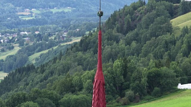 Red spire of Ringebu Stave Church rises proudly, its cross overlooking the serene Norwegian valley