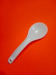 A white rice spoon against an orange background. 