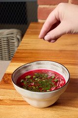 Hand Sprinkling Fresh Aromatic Herbs Generously Over a Colorful Beetroot Soup Bowl