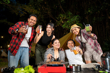 Indonesian southeast asian people relaxing together outdoors and enjoying refreshing drinks while cooking sliced beef on a grill pan. The scene of the lifestyle of enjoying food in a natural setting