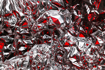 Close up of crumpled silver foil with red reflections creating an abstract textured background. Shiny metallic surface with vibrant contrast and modern artistic look.