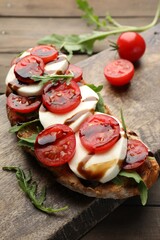 Delicious sandwich with mozzarella cheese, balsamic sauce, tomatoes and arugula on wooden table, closeup