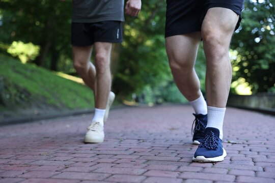 Young man running with professional personal trainer outdoors, closeup