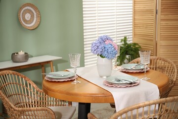 Stylish setting with plates and vase of flowers on wooden table in dining room. Interior design