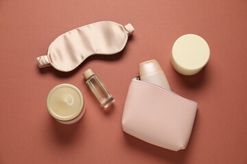 Bag with cosmetic products and sleeping mask on brown background, flat lay