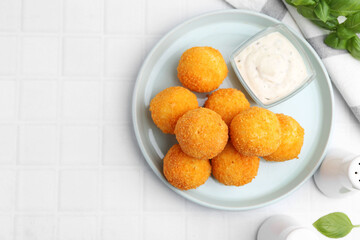 Delicious fried croquette balls, sauce and basil on light tiled table, flat lay. Space for text