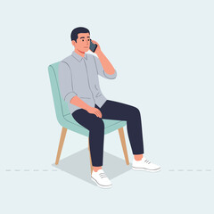 A young man in casual attire sitting on a modern chair while talking on his mobile phone.