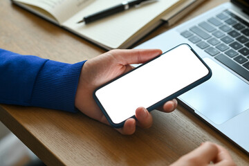Person holding smartphone with blank screen mockup near laptop and notebook for digital marketing 100