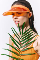 Young woman in orange outfit and visor holding a palm leaf, showcasing vibrant colors and summer vibe with a cheerful expression.