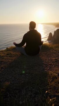 Man Meditating in Yoga Pose at Cliffside Overlooking Ocean at Sunset in Peaceful Scene with Warm Sunlight and Tranquil Water View