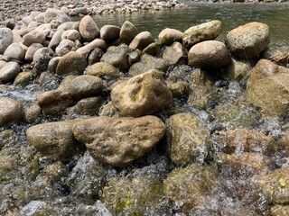 Close-up view of water flowing over a rocky riverbed, with smooth stones and pebbles in clear water