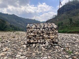 Gabion structure made of stones on a rocky riverbed with hills in the background
