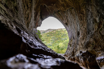 Exploring natural rock cave overlooking green valley landscape